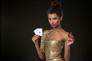 Woman winning - Young woman in a classy gold dress holding two aces and two red chips, a poker of aces card combination. photo