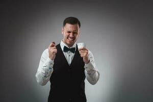 Young man in shirt and waistcoat shows his cards and holds poker chips in his hands, studio shot photo