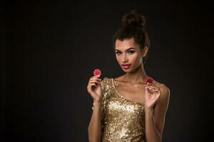 Woman winning - Young woman in a classy gold dress holding two red chips, a poker of aces card combination. photo