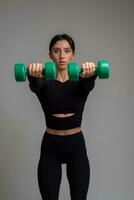 Athletic woman doing dumbbell front raise with both hands on grey background photo