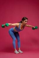 Athletic girl doing shoulders exercise on maroon background photo