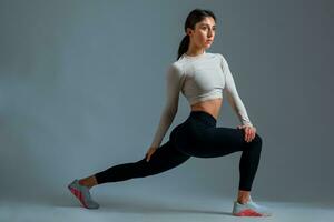 Sportswoman doing stretching lunges with twisting of body on grey background photo