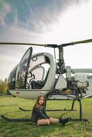 interpolación niña sentado en verde césped de volador campo cerca helicóptero foto