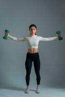 Girl performing set of shoulder exercises with dumbbells on grey background photo