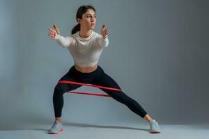Woman performing resistance band side lunges on grey background photo
