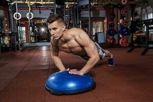 Muscular man doing push up on bosu ball at crossfit gym photo