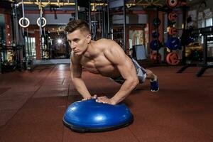 muscular hombre haciendo empujar arriba en bosu pelota a crossfit gimnasio foto