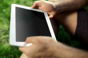 Young man using and typing tablet computer in summer grass. photo