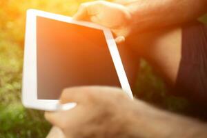 Young man using and typing tablet computer in summer grass. photo