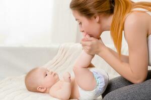 Mother and child on a white bed. Mom and baby girl in diaper playing in sunny bedroom. photo