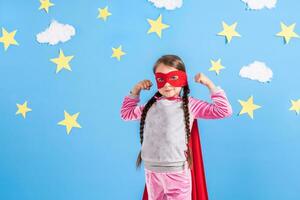 seis año rubia niña vestido me gusta superhéroe teniendo divertido a hogar. niño en el antecedentes de brillante azul pared. foto