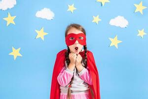 pequeño niño obras de teatro superhéroe niño en el antecedentes de brillante azul pared con blanco nubes y estrellas . niña poder concepto. foto