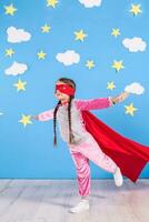 Six year blonde girl dressed like superhero having fun at home. Kid on the background of bright blue wall. photo