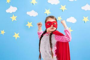 Six year blonde girl dressed like superhero having fun at home. Kid on the background of bright blue wall. photo