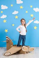 Little dreamer girl playing with a cardboard airplane at the studio with blue sky and white clouds background. photo