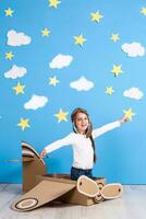 Little dreamer girl playing with a cardboard airplane at the studio with blue sky and white clouds background. photo