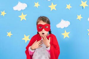 Little child plays superhero. Kid on the background of bright blue wall with white clouds and stars . Girl power concept. photo