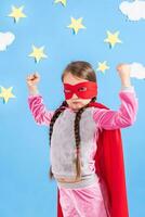 Six year blonde girl dressed like superhero having fun at home. Kid on the background of bright blue wall. photo