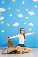 Little dreamer girl playing with a cardboard airplane at the studio with blue sky and white clouds background. photo