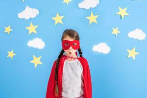 Little child plays superhero. Kid on the background of bright blue wall with white clouds and stars . Girl power concept. photo