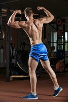 Man standing strong in the gym and flexing muscles photo