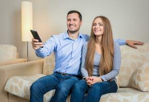 Portrait of happy couple sitting on sofa watching television together photo