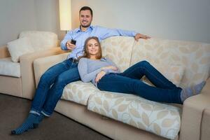 Happy couple sitting on sofa watching television together photo