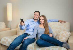 Portrait of happy couple sitting on sofa watching television together photo