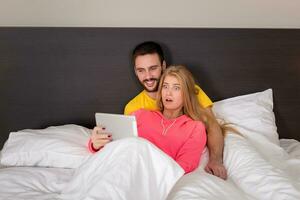 Young Sweet Couple at Bed Watching Something on Tablet Gadget photo