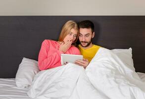 Young Sweet Couple at Bed Watching Something on Tablet Gadget photo