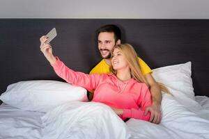 joven contento Pareja en cama haciendo selfie con teléfono cámara. foto