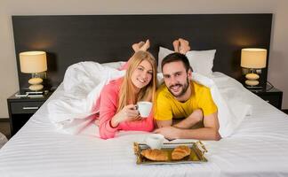 contento joven Pareja teniendo desayuno bandeja en cama a hogar foto