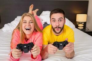 Happy young couple having fun playing videogames in bed photo