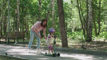 Mama unterrichtet Tochter zu Reiten ein Roller im das Park im Sommer. video