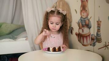un pequeño niña come un pastel y disfruta su cumpleaños. video