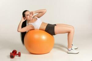 Young beautiful sportswoman with dumbbells exercising on fitball photo