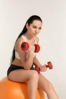 Young beautiful sportswoman with dumbbells exercising on fitball photo