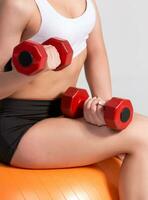 Sportswoman with dumbbells exercising on fitball photo