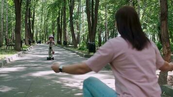 Mom teaches daughter to ride a scooter in the park in summer. video