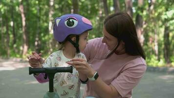 Mama unterrichtet Tochter zu Reiten ein Roller im das Park im Sommer. video