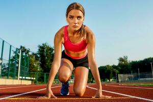 joven mujer atleta a comenzando posición Listo a comienzo un carrera en pista. foto