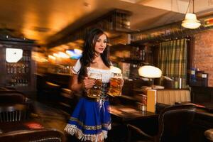 Beautiful female waitress wearing traditional dirndl and holding huge beers in a pub. photo
