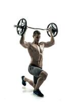 Muscular man standing on knee, holding barbell over his head photo