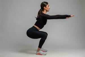 Side view of girl doing squats on grey background photo