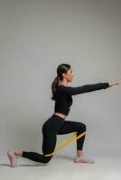 Girl performing lunges with resistance band on grey background photo