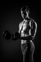 Handsome man showing perfect body with dumbbells on black backgr photo