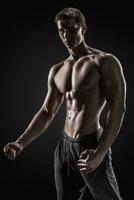 Sexy shirtless bodybuilder posing, looking at camera on black background. photo