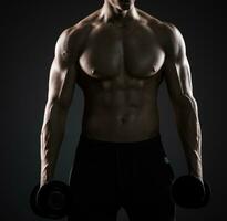 Muscular man showing perfect body with dumbbells on black background photo