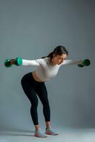 Athletic girl doing reverse fly with dumbbells on grey background photo