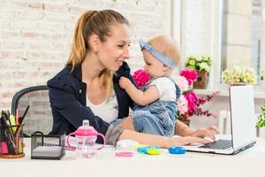 Mom and businesswoman working with laptop computer at home and playing with her baby girl. photo